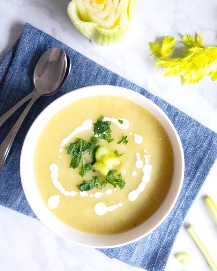 cream of celery soup in a bowl drizzled with yogurt and garnished with celery and herbs.