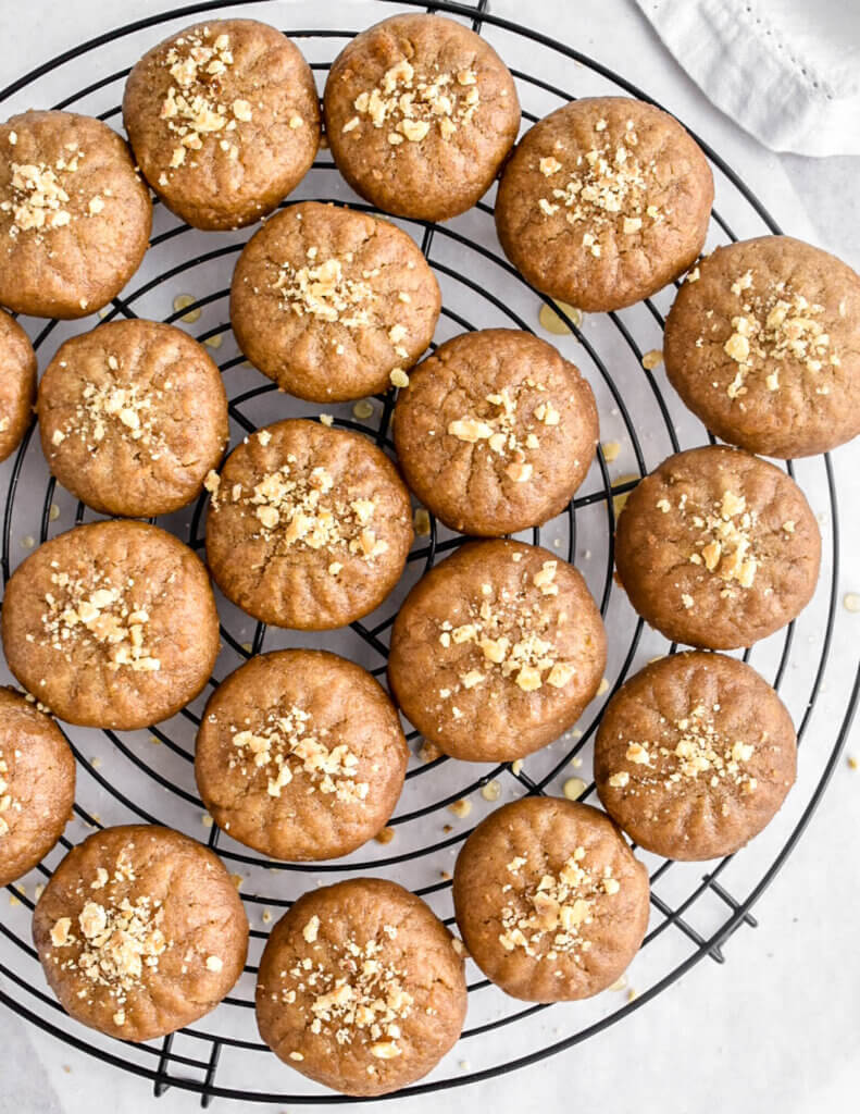 Melomakarona cookies drenched in honey and topped with crushed walnuts on a black circular rack.