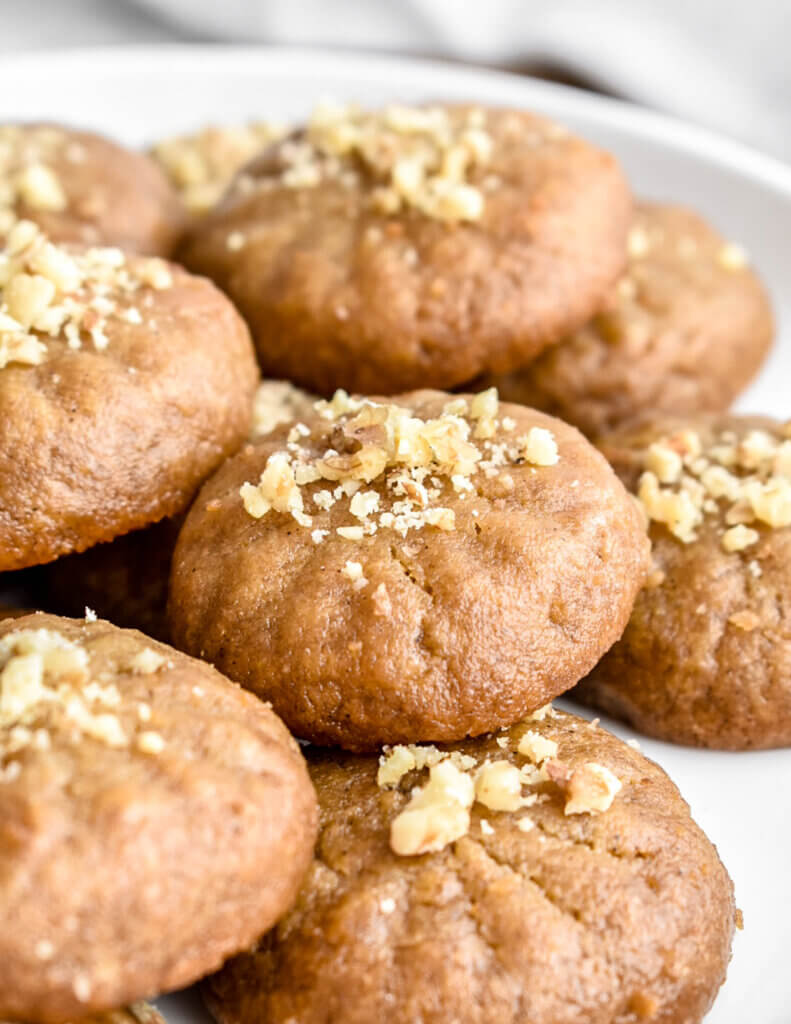 Closeup of melomakarona cookies topped with walnut piled together on a platter.