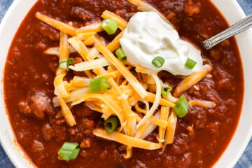 A bowl of Turkey Chili topped with shredded cheddar cheese, sour cream, and green onions and set down on a folded blue cloth napkin.