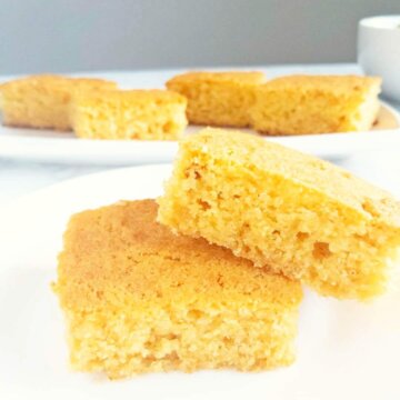 Two stacked pieces of Easy Homemade Cornbread set in front of a platter of cornbread.