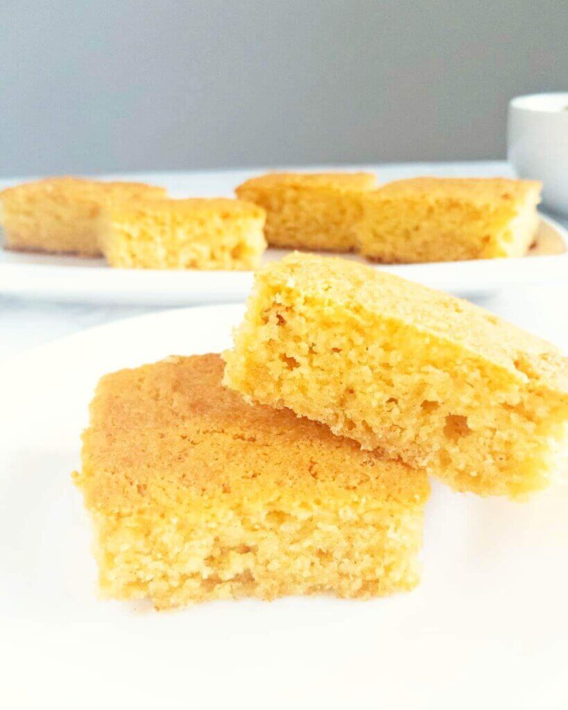 Two stacked pieces of Easy Homemade Cornbread set in front of a platter of cornbread.