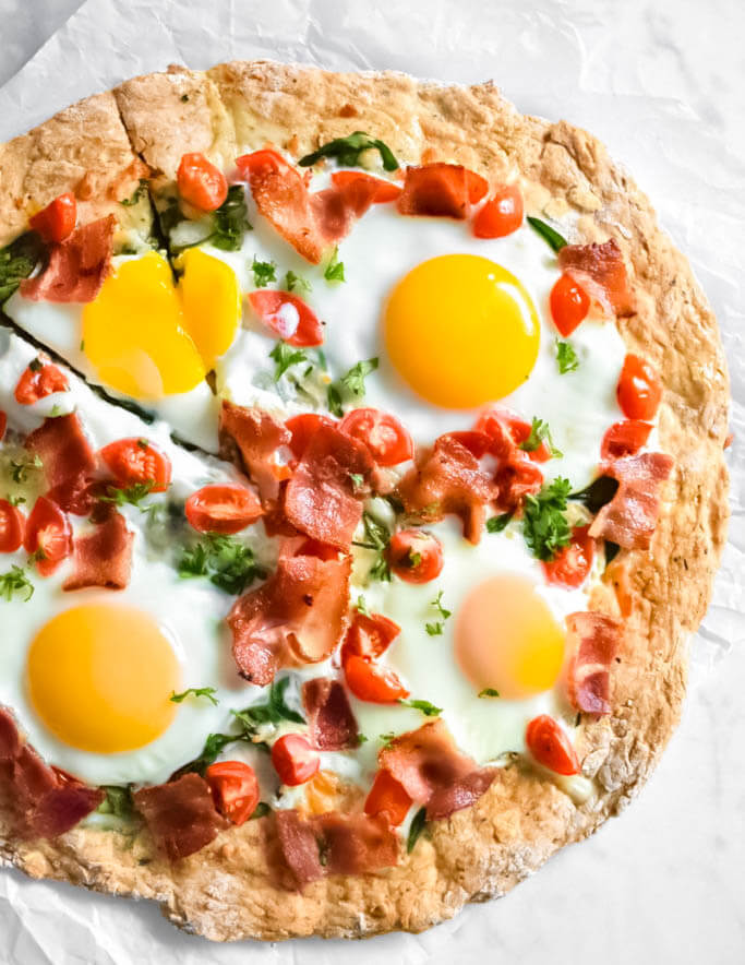 Breakfast Pizza topped with cracked eggs, bacon and chopped tomatoes.