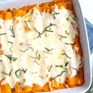 A square baking dish filled with Creamy Squash, Spinach & Turkey Cannelloni topped with melted mozzarella and sage.