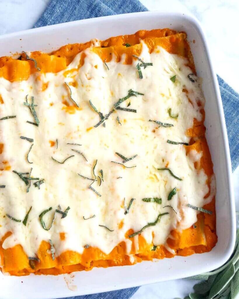 A square baking dish filled with Creamy Squash, Spinach & Turkey Cannelloni topped with melted mozzarella and sage.