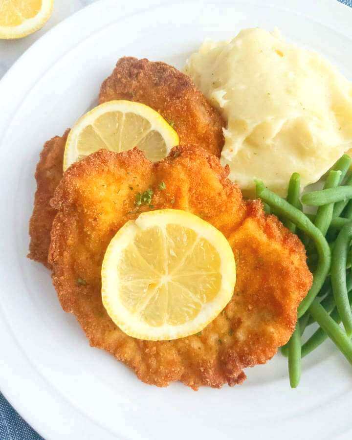 Plate of pork schnitzel served with mashed potatoes and green beans.