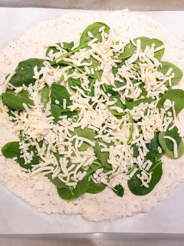 Pizza dough topped with spinach and mozzerella.