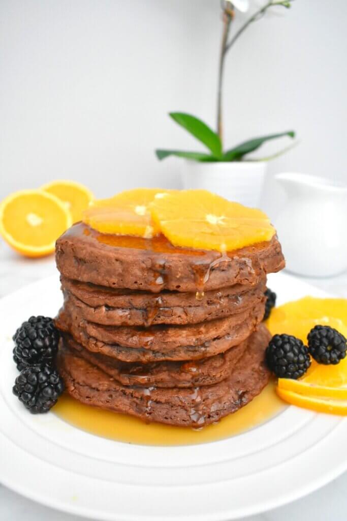 A stack of Chocolate Orange Pancakes topped with orange slices and drizzled with maple syrup.