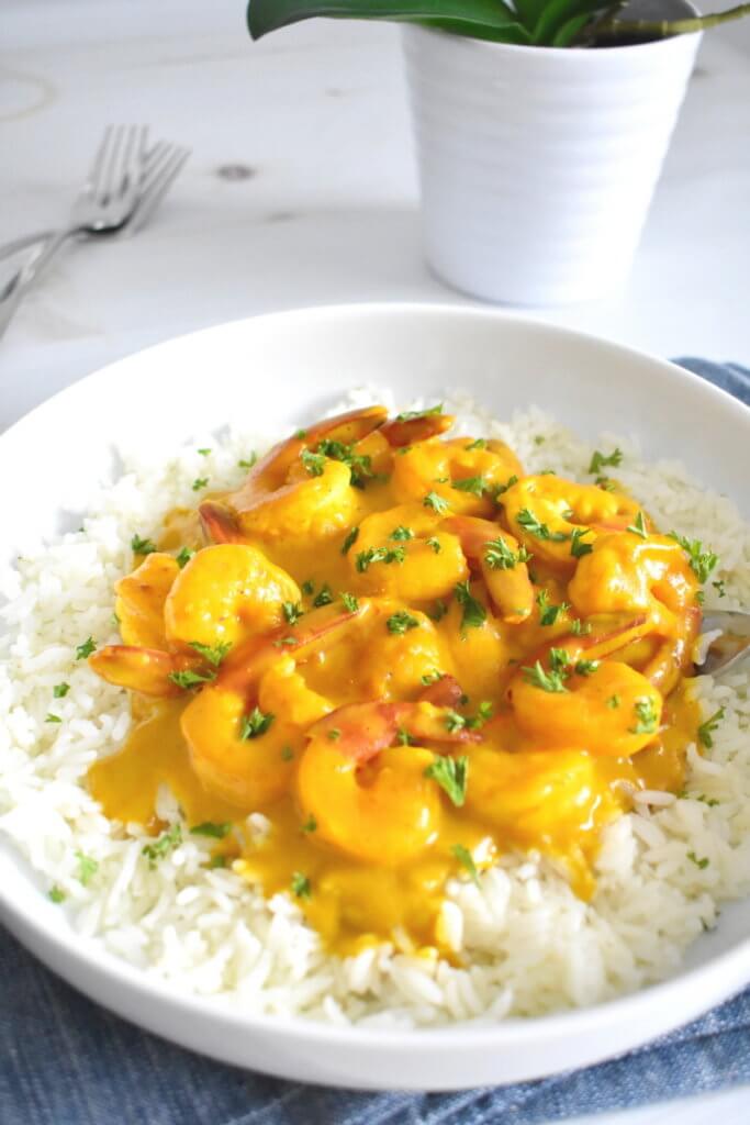 Creamy Coconut Turmeric Shrimp plated over rice on a kitchen table.