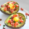 baked avocado eggs topped with chopped tomatoes and fresh herbs