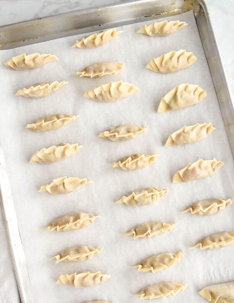 A tray of pork pot stickers on a parchment lined baking sheet.