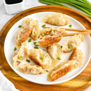 A plate of pork pot stickers served with soy sauce and sprinkled with green onion and sesame seeds.