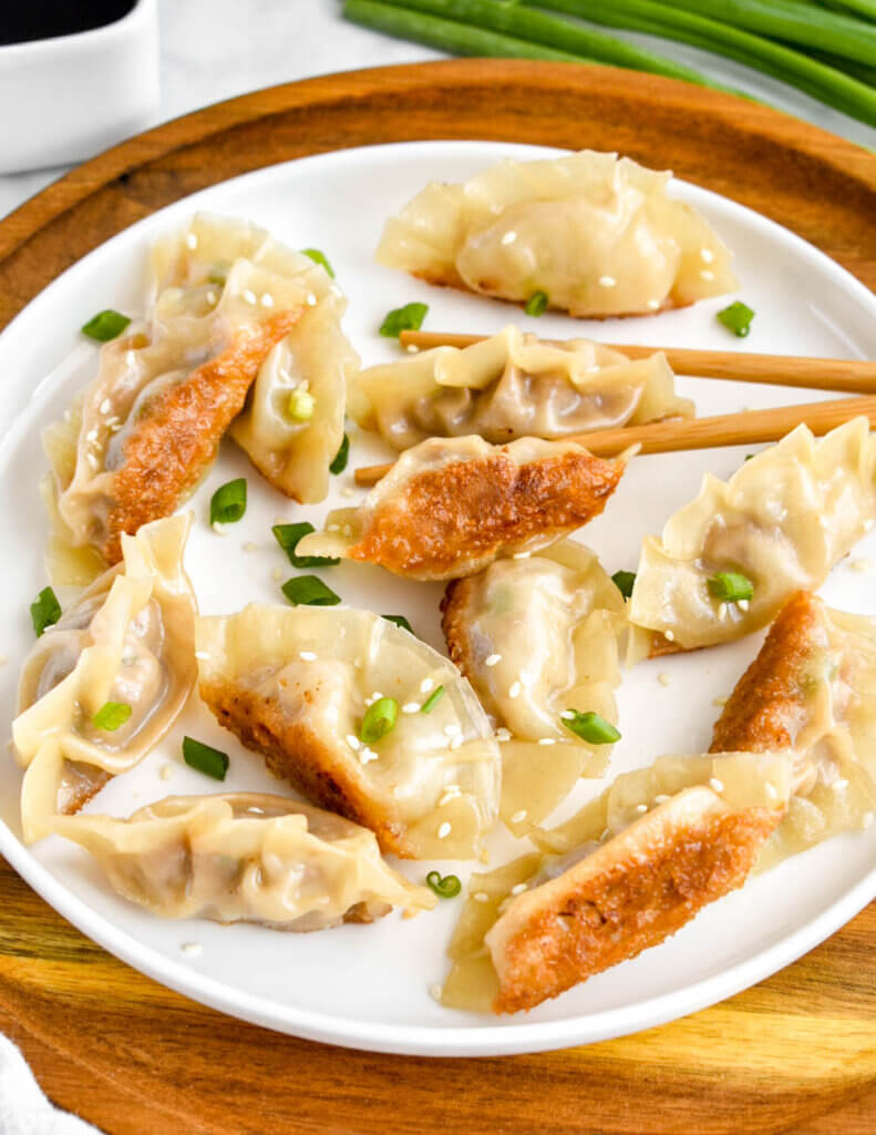Closeup of a plate of pot stickers with crispy golden bottoms and sprinkled with green onion and sesame seeds.