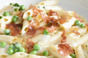 A bowl of creamy penne pasta topped with peas and crispy prosciutto.