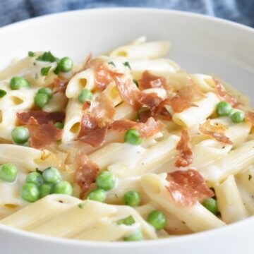 A bowl of creamy penne pasta topped with peas and crispy prosciutto.