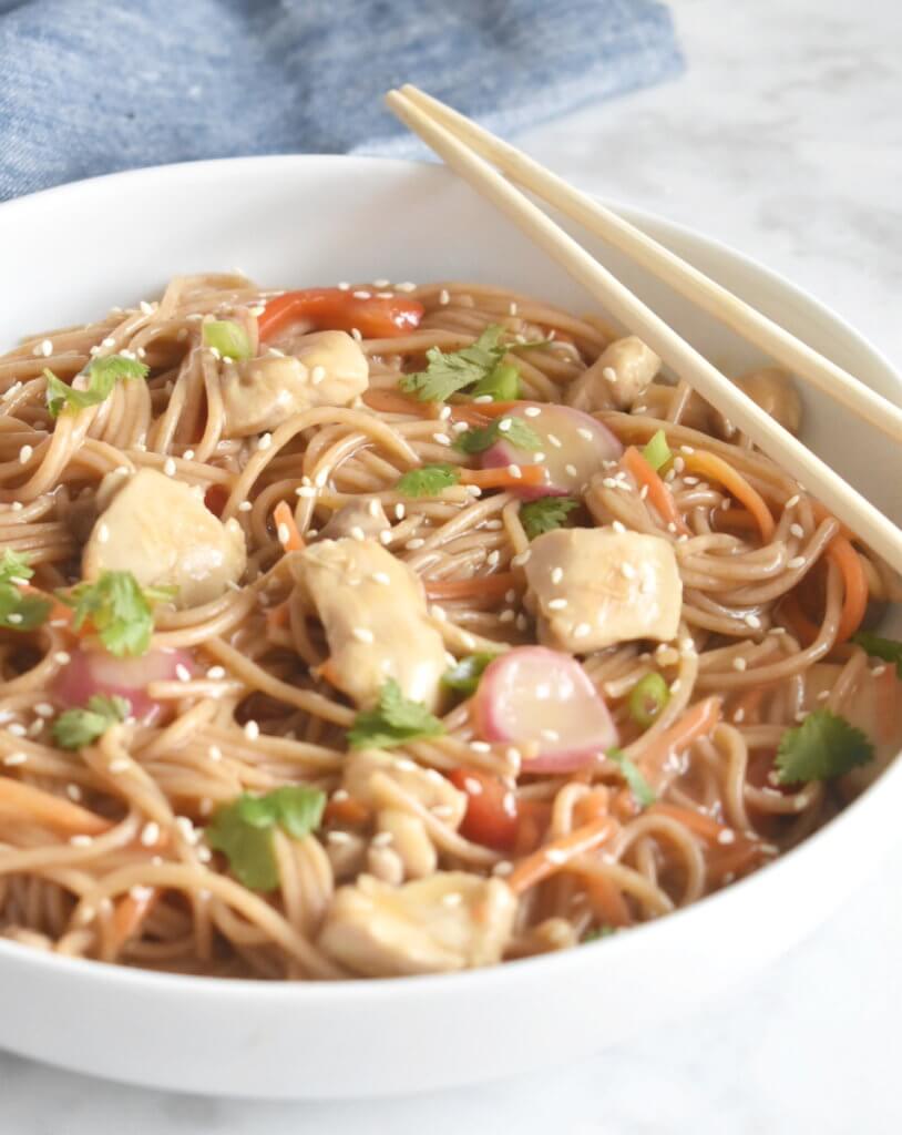 Closeup of a bowl of noodles covered in a sweet citrus sauce with pieces of chicken and vegetables.