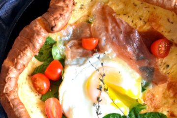 Closeup of a Savory Dutch Baby in a cast iron skillet topped with spinach, cherry tomatoes and a fried egg.