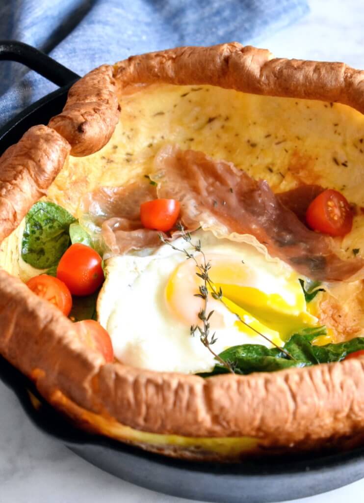 Closeup sideview of a Savory Dutch Baby topped with spinach, cherry tomatoes and a fried egg.