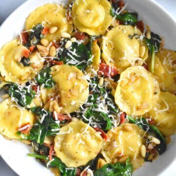 A plate of ravioli with spinach, sundried tomatoes, and artichokes.