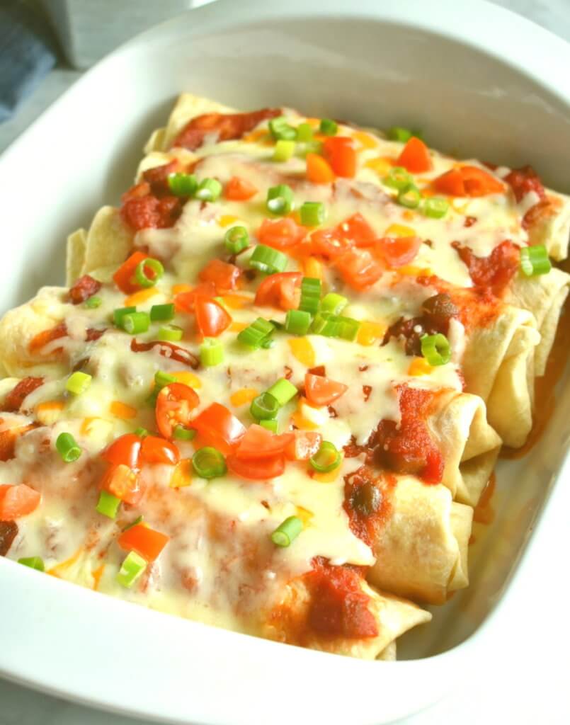 Baking dish with chicken enchiladas covered in salsa and melted cheese.