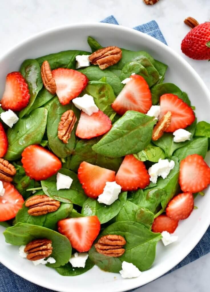 A bowl of Strawberry Spinach Salad topped with sliced strawberries, pecans and goat cheese.