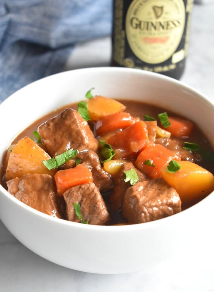 A bowl of Irish Beef Stew next to a bottle of guinness beer.