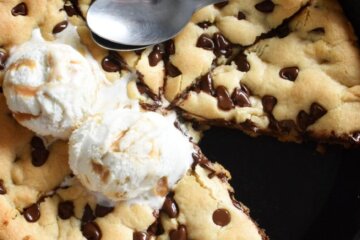 Sliced chocolate chip skillet cookie in a cast iron skillet topped with ice cream.