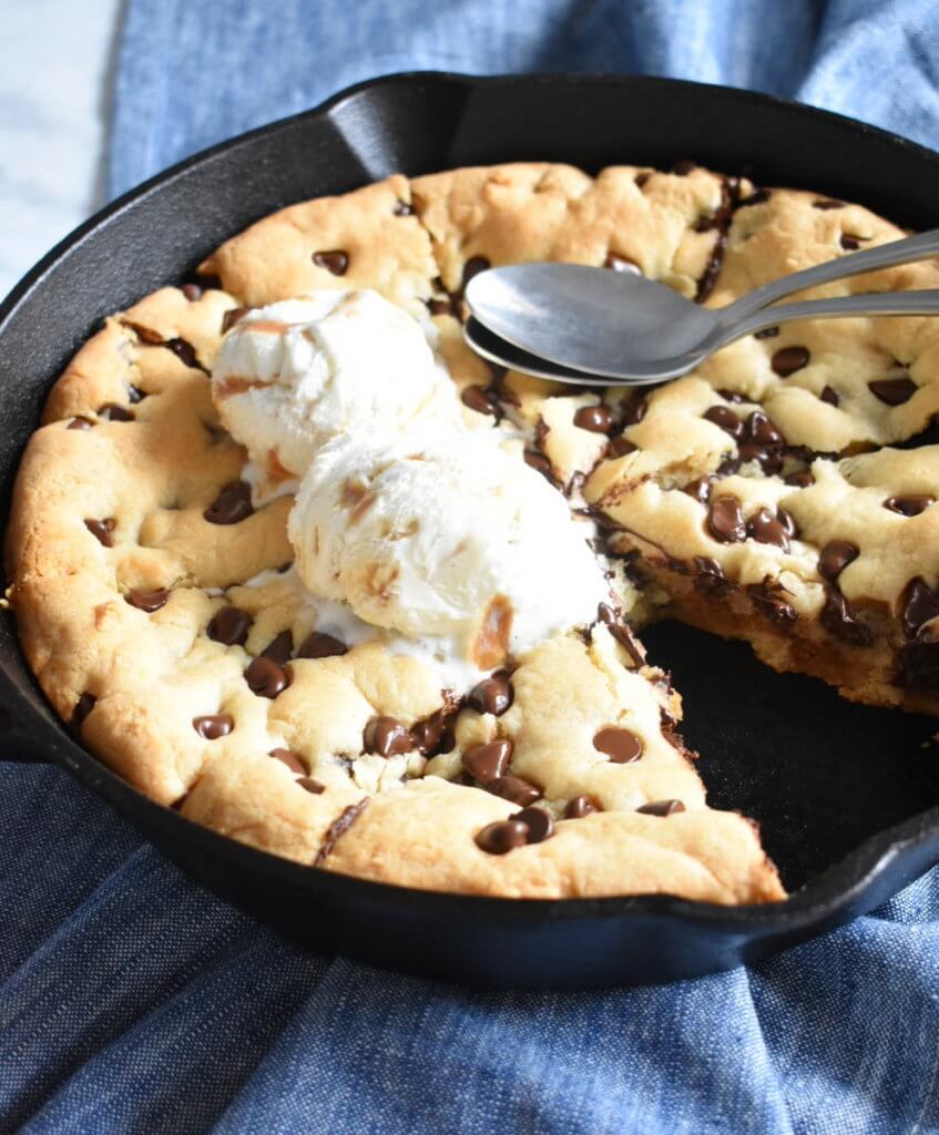 chocolate chip skillet cookie in a cast iron skillet served with spoons.