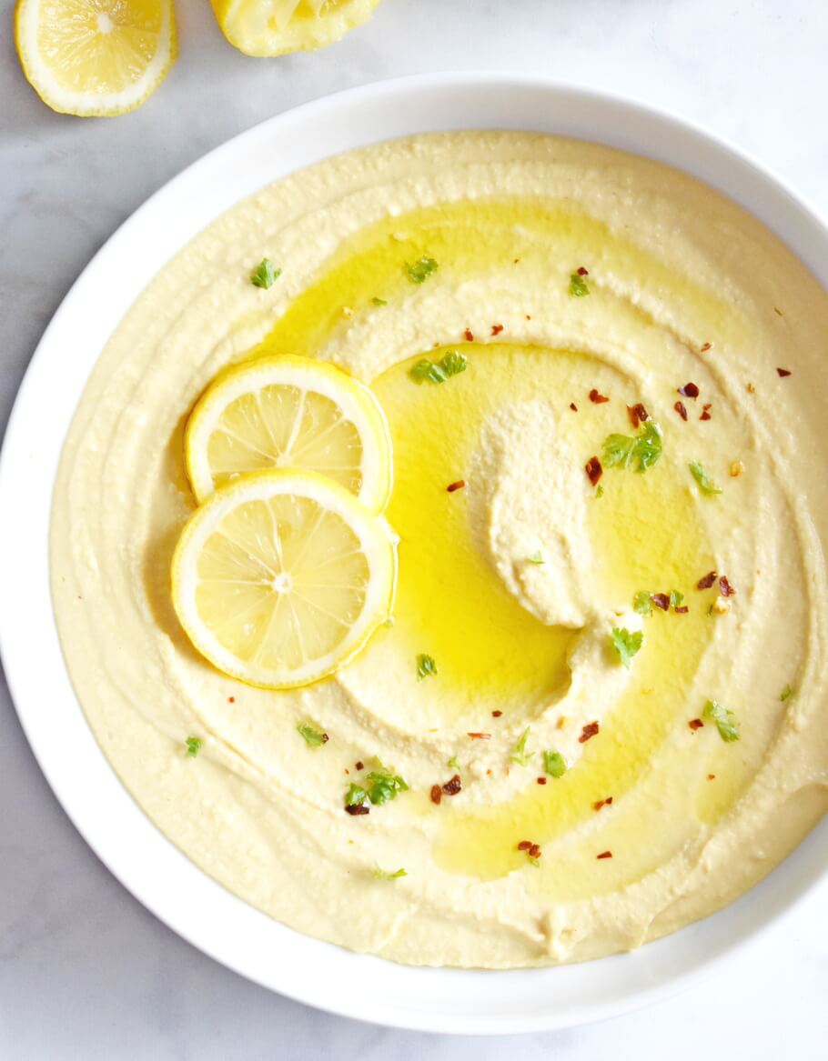 Bowl of hummus topped with olive oil and lemon slices.