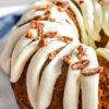 Closeup of a carrot bundt cake drizzled with cream cheese frosting and sprinkled with chopped pecans.
