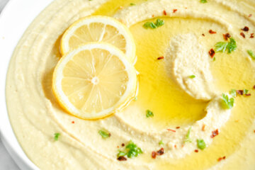 Hummus served in a white bowl and topped with olive oil, lemon slices and red pepper flakes.