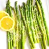 A square platter of Roasted Asparagus with Parmesan served with lemon slices.