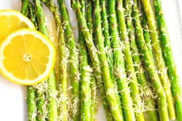 A square platter of Roasted Asparagus with Parmesan served with lemon slices.