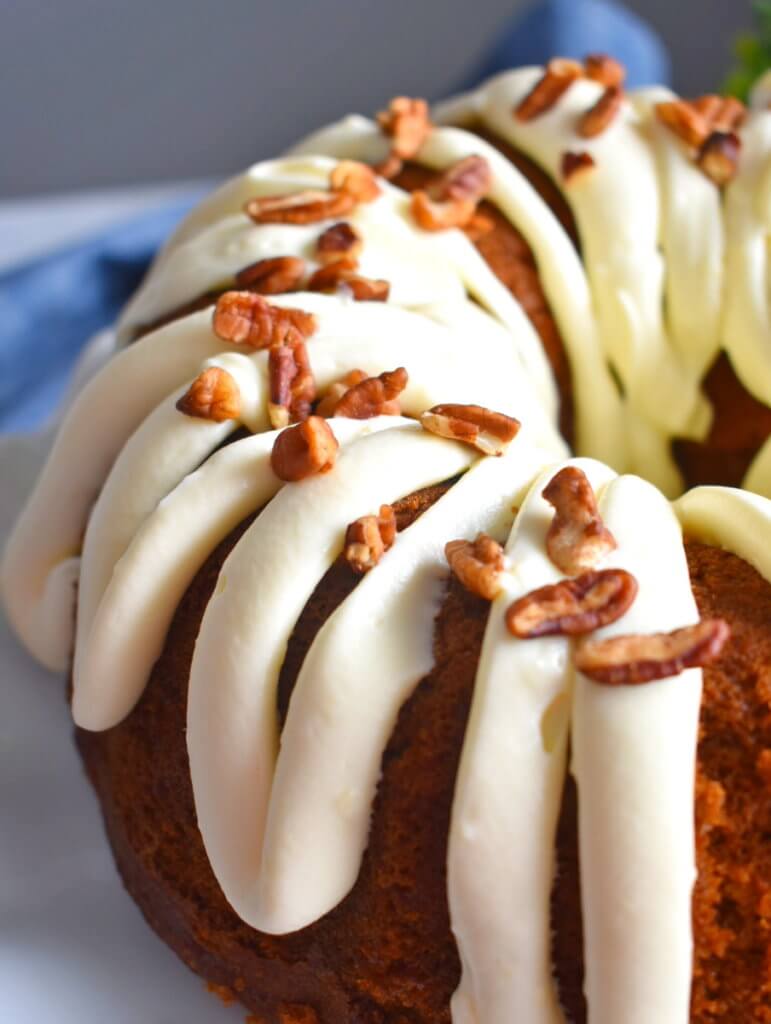 A carrot cake bundt cake with cream cheese frosting and sprinkle of pecans.