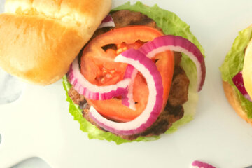 Classic Homemade Hamburger topped with lettuce, tomatoes and red onions set on a serving platter.