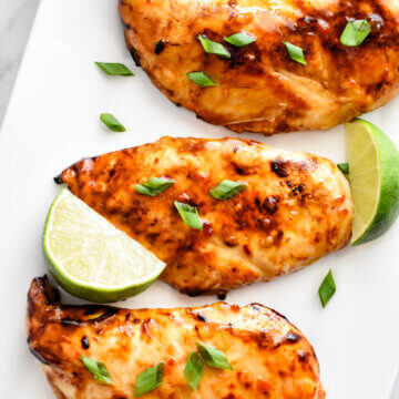 Three Thai Sweet Chili Chicken breasts sprinkled with cilantro on a rectangular platter with lime wedges.