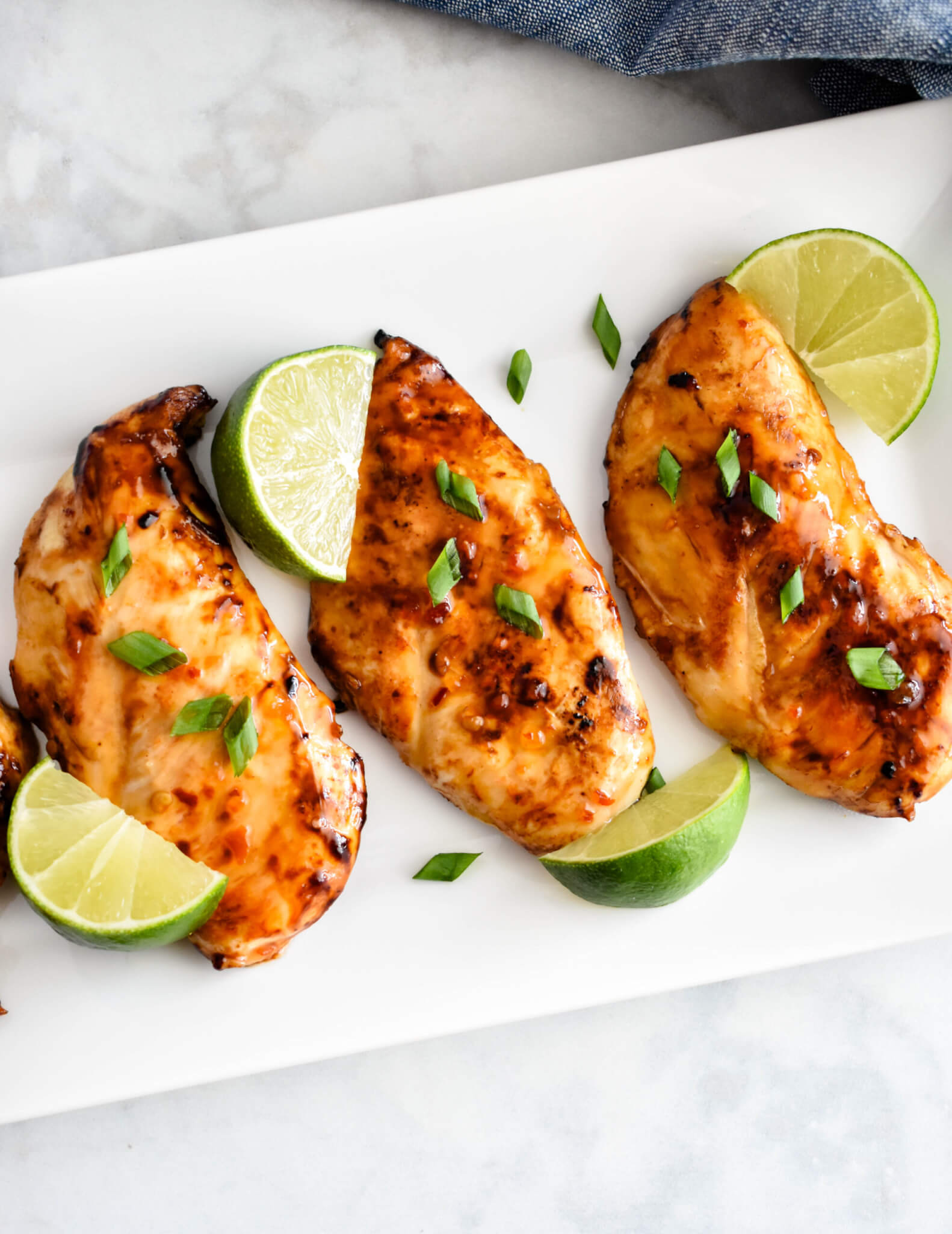 Overhead shot of Thai Sweet Chili Chicken breasts on a rectangular platter served with lime wedges.