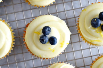 Topview of Lemon Blueberry Cupcakes with Lemon Cream Cheese Frosting and fresh bluebrries on top on a cooling rack.