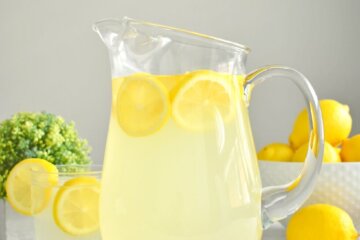 A pitcher of lemonade with lemon slices next to a bowl of lemons.