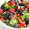 A bowl of arugula salad topped with blackberries, blueberries, strawberries and raspberries.