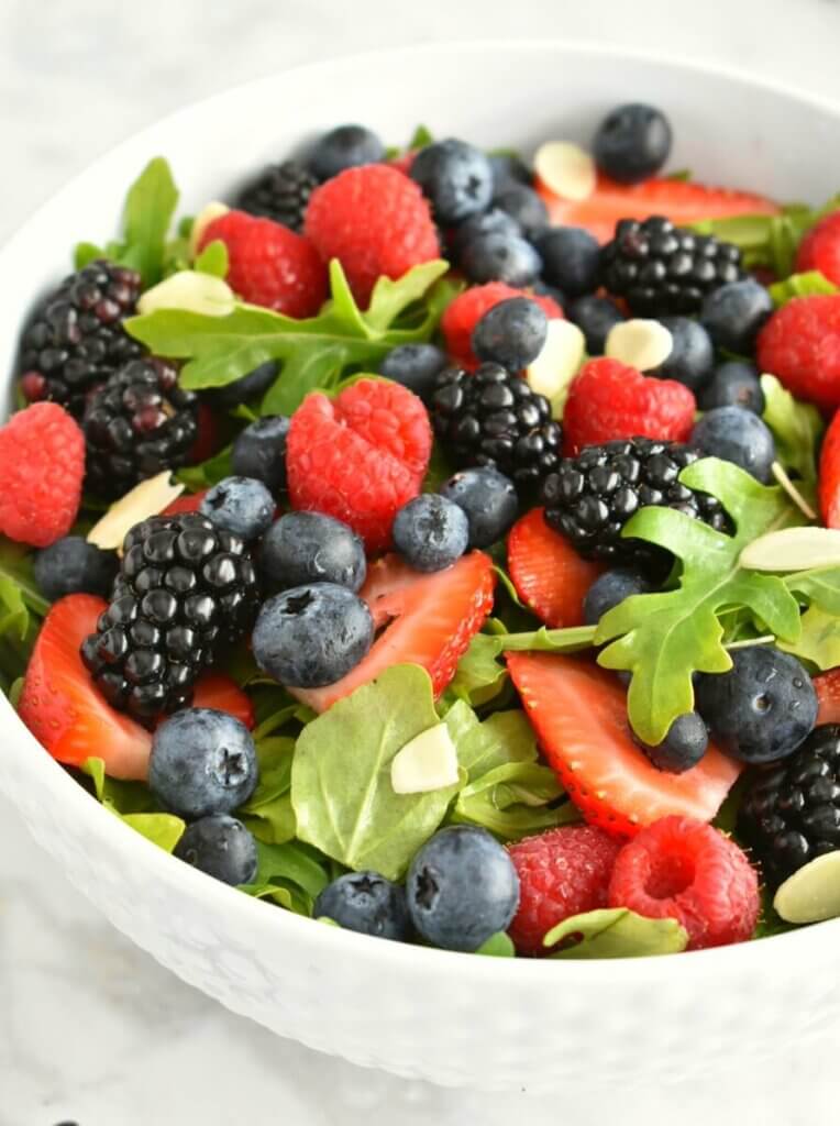 A bowl of arugula salad topped with blackberries, blueberries, strawberries and raspberries.