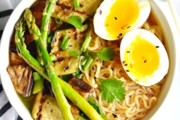 A bowl of ramen topped with grilled asparagus, eggplant and zuchini and a jammy egg.