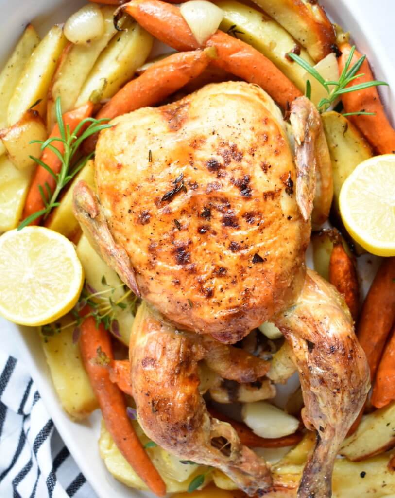 Closeup of a roasted chicken on a bed of potatoes and roasted carrots.