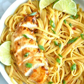 Close up of Sweet Chili Chicken on a baed of noodles with lime wedges.