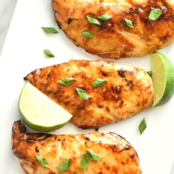 Thai Sweet Chili Chicken sprinkled with cilantro on a rectangular platter with lime wedges.
