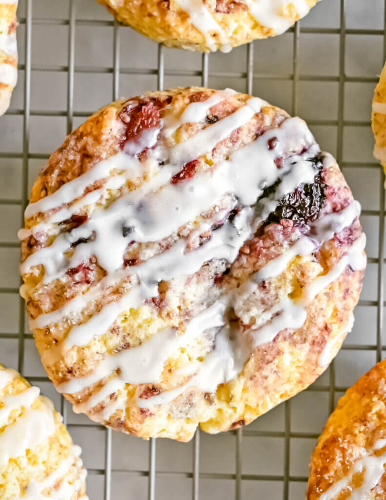 A blackberry scone drizzled with icing on a cooling rack.