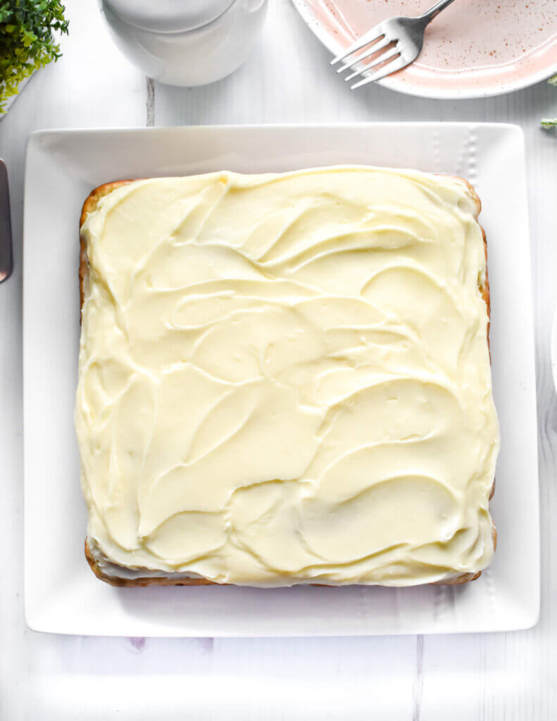 A square Healthy Banana Cake with swirled cream cheese frosting on a square serving platter.