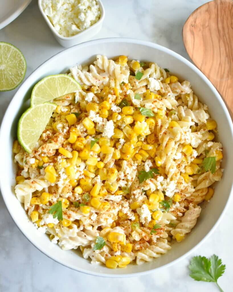 Topview of a bowl of Healthy Mexican Street Corn Pasta Salad topped with cilantro and lime wedges set on a kitchen counter.