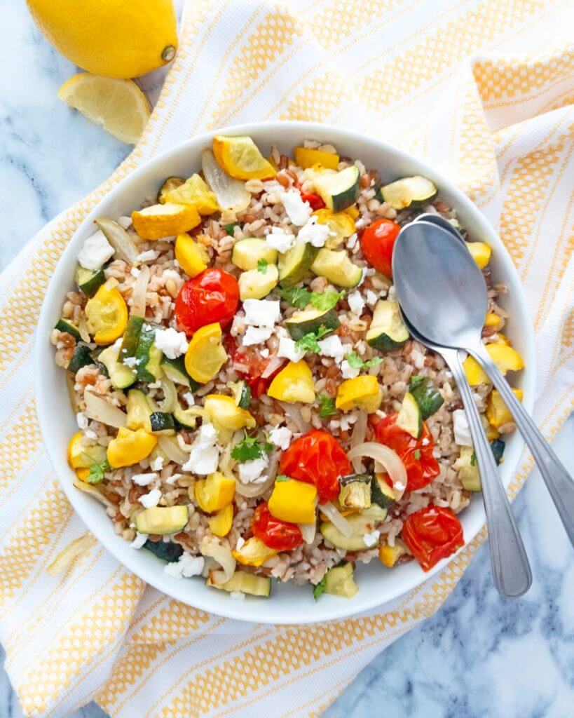 A bowl of Mediterranean Grain Salad with Roasted Summer Vegetables with serving spoons.
