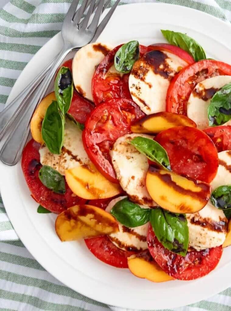 A plate of Peach Caprese Salad with tomatoes, peaches, and mozzarella.